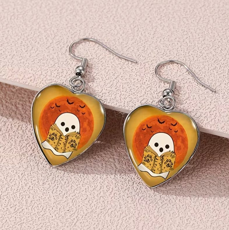 Heart-shaped earrings featuring a ghost reading under an orange harvest moon