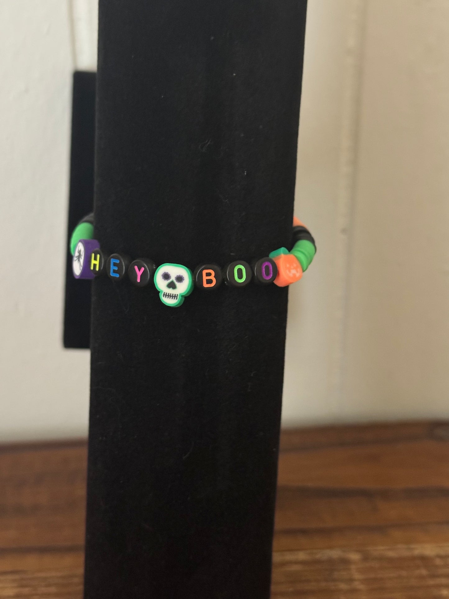 Black bracelet with colorful beads spelling 'HEY BOO' on a wooden surface.