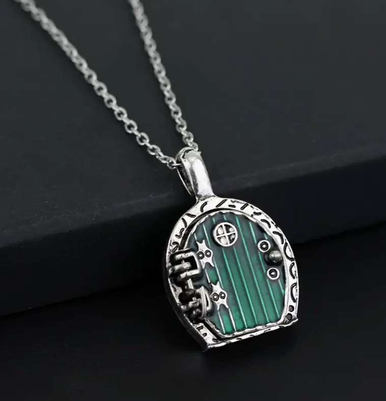 A detailed green hobbit door necklace with a round, rustic design. The door opens and closes with a magnetic closure, revealing a hidden space inside.