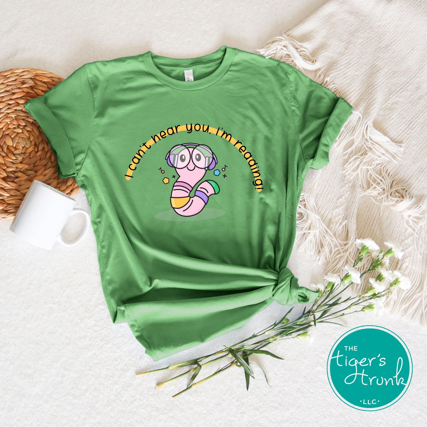 Green t-shirt with a cartoon design on a textured surface with a mug and flowers.
