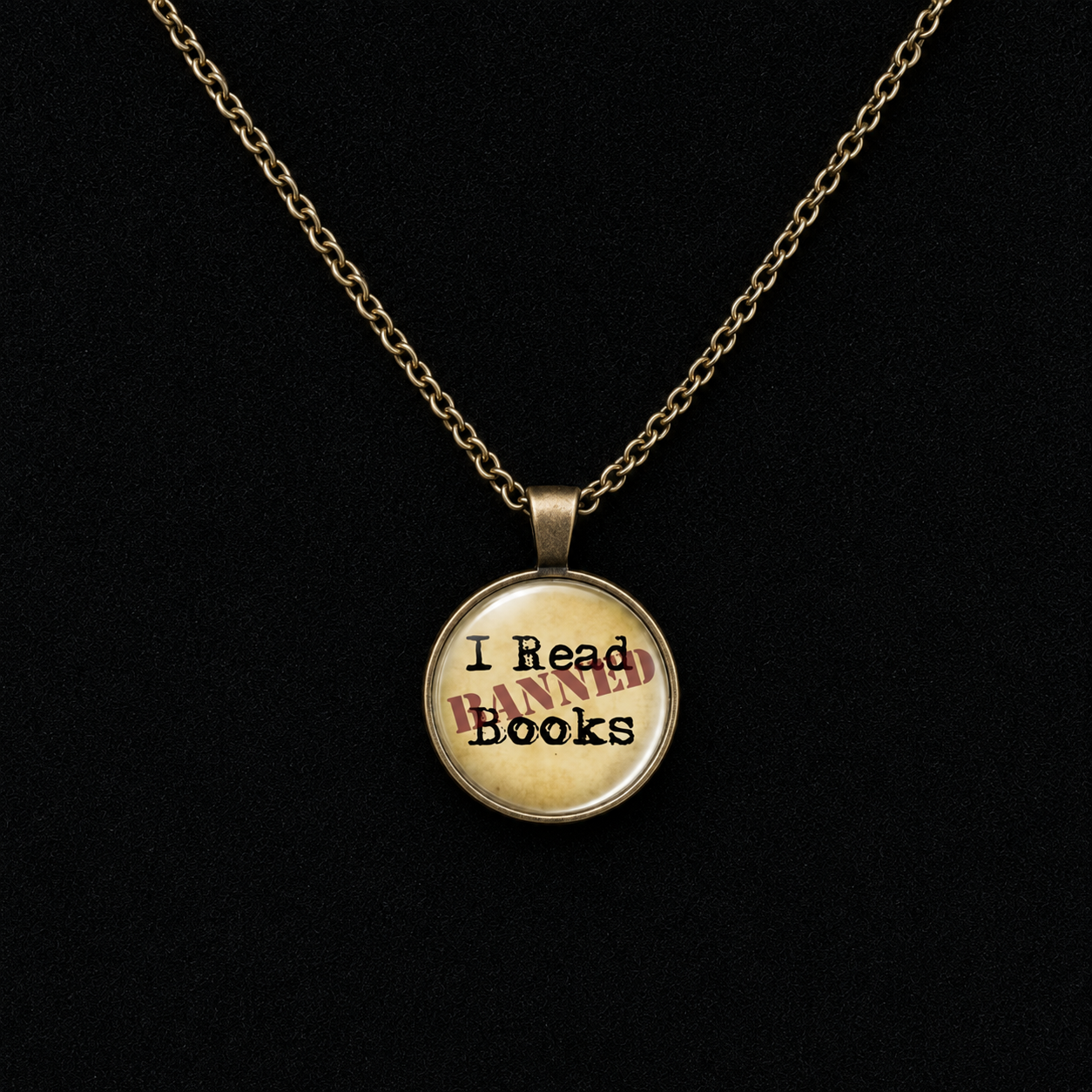 A gold chain necklace with a round pendant featuring a vintage-style beige background and the text 'I Read BANNED Books' in black and red, displayed against a solid black background.