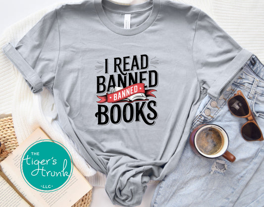 Gray t-shirt with 'I Read Banned Books' text, sunglasses, coffee cup, and book on a white surface.