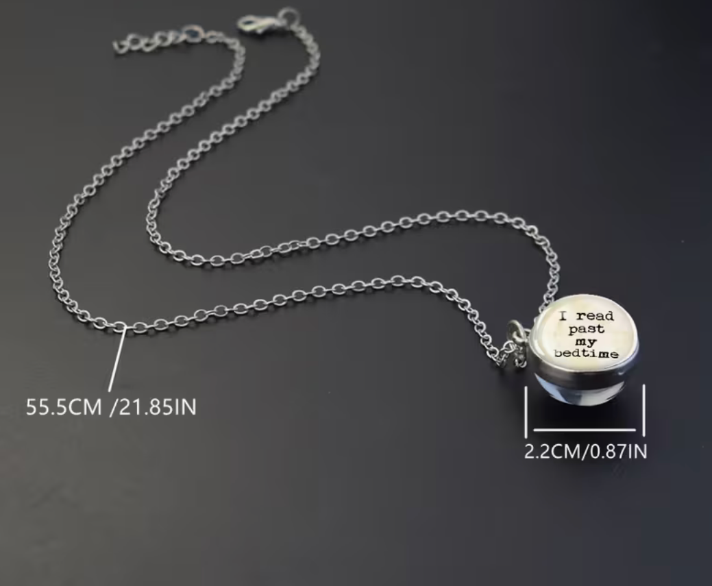 A silver chain necklace with a round pendant engraved with the phrase 'i read past my bedtime', shown on a dark background with measurement labels indicating 55.5 cm chain length and 2.