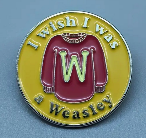 Enamel pin reading I Wish I Was a Weasley with a red sweater and yellow background