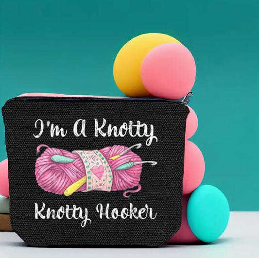 Black pouch with pink yarn and text, surrounded by colorful yarn balls on a teal background