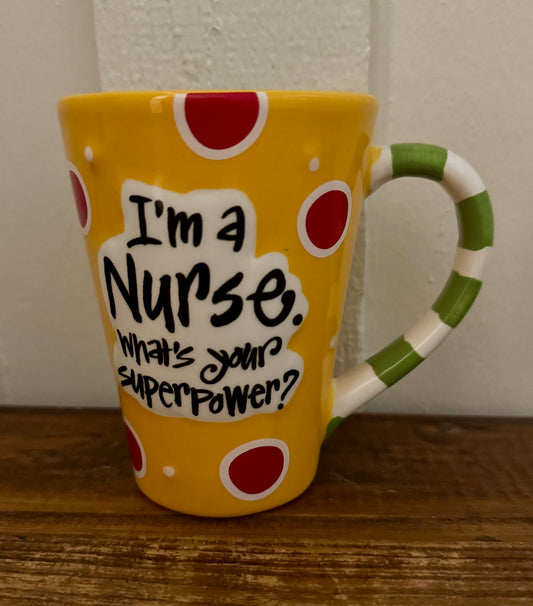 Yellow mug with red polka dots and a green handle, featuring text 'I'm a Nurse. What's your superpower?' on a wooden surface.