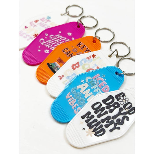 Assorted inspired vintage hotel motel keychains with retro designs and uplifting phrases displayed on a white background