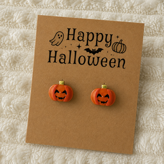 Orange jack-o’-lantern pumpkin stud earrings with black smiling faces and gold-tone stems displayed on a Halloween earring card.