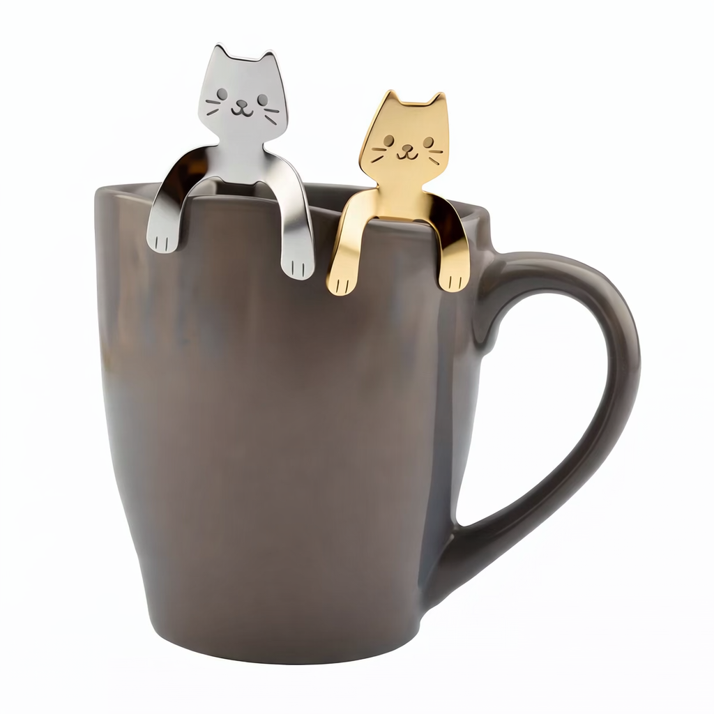 Silver and gold stainless steel kawaii cat spoons hanging on the rim of a gray coffee mug with paws hooked over the edge.
