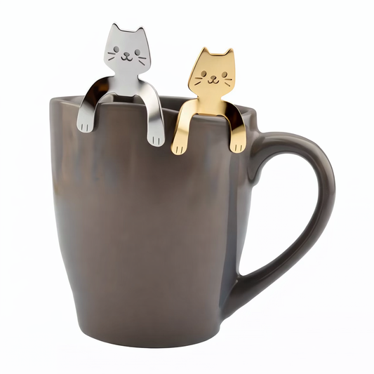 Silver and gold stainless steel kawaii cat spoons hanging on the rim of a gray coffee mug with paws hooked over the edge.