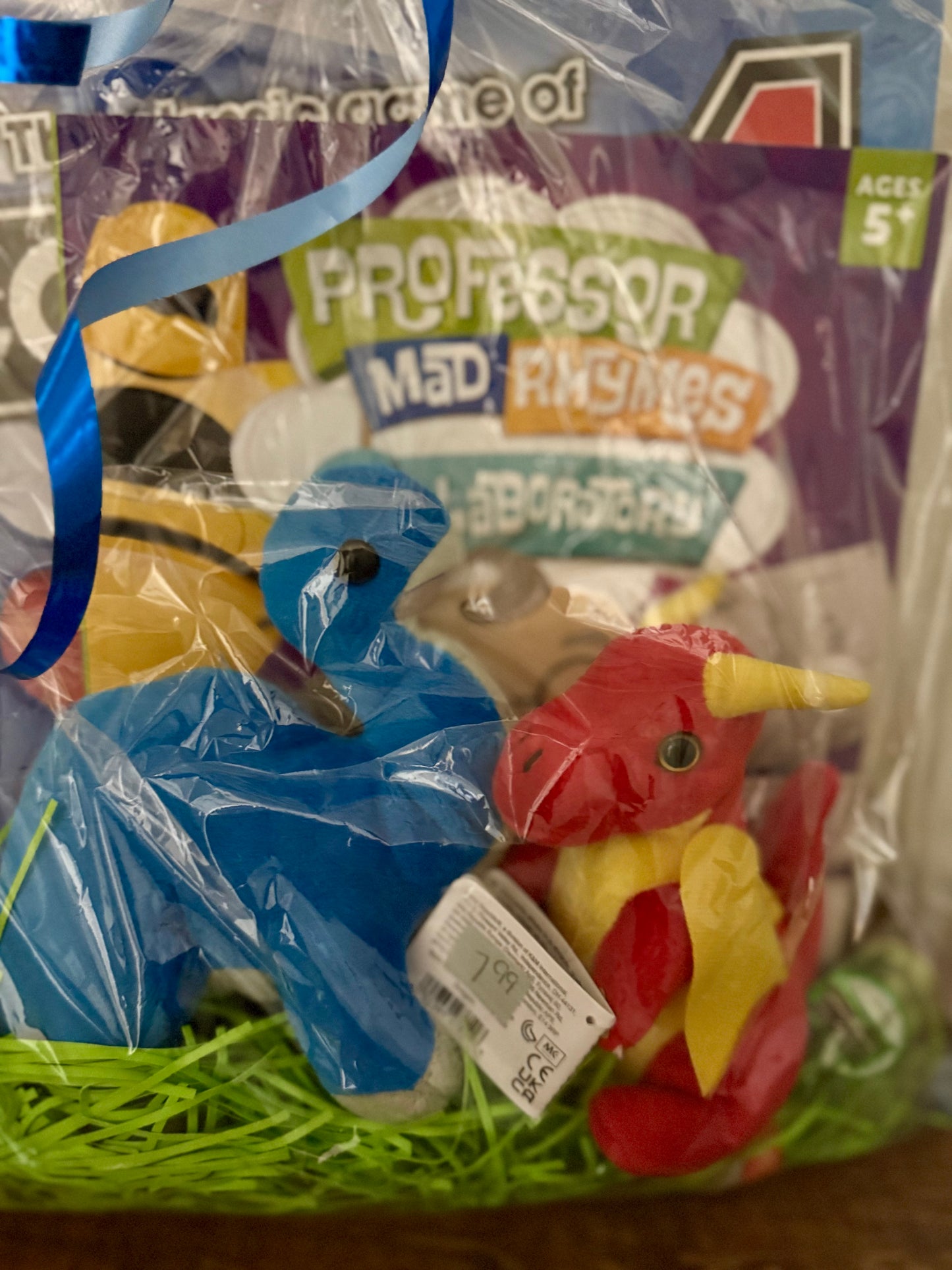Close-up of the kids activity gift bag displaying the stuffed blue dinosaur and red dragon with the Connect 4 game and Professor Mad Rhymes coloring book behind them.