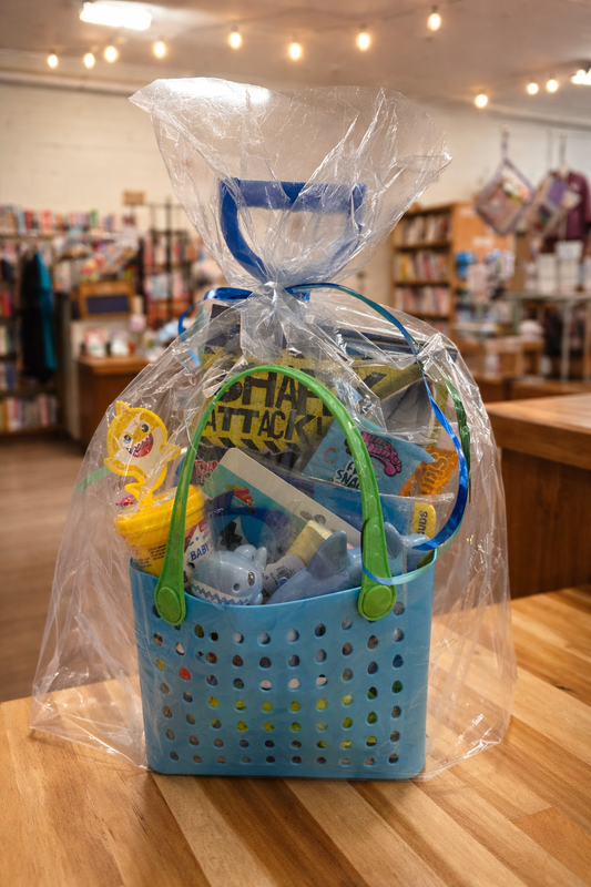 Kids shark-themed summer gift basket in blue tote bag with toys and Shark Attack book wrapped in clear gift wrap