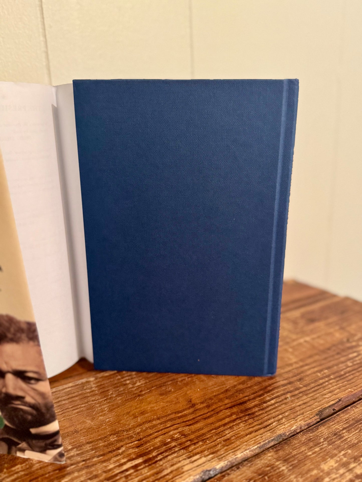 Blue notebook on a wooden surface with a white book and photo in the background