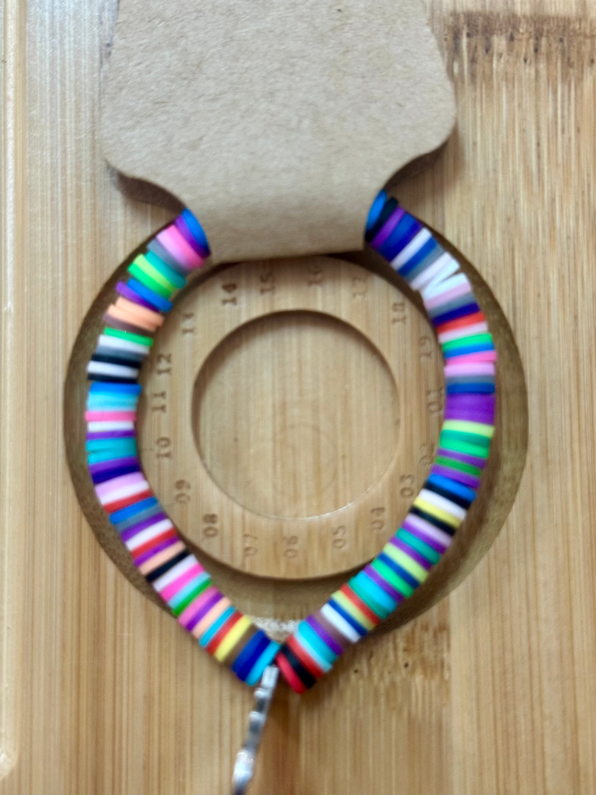 Colorful striped bracelet on a wooden surface with a ruler for scale.