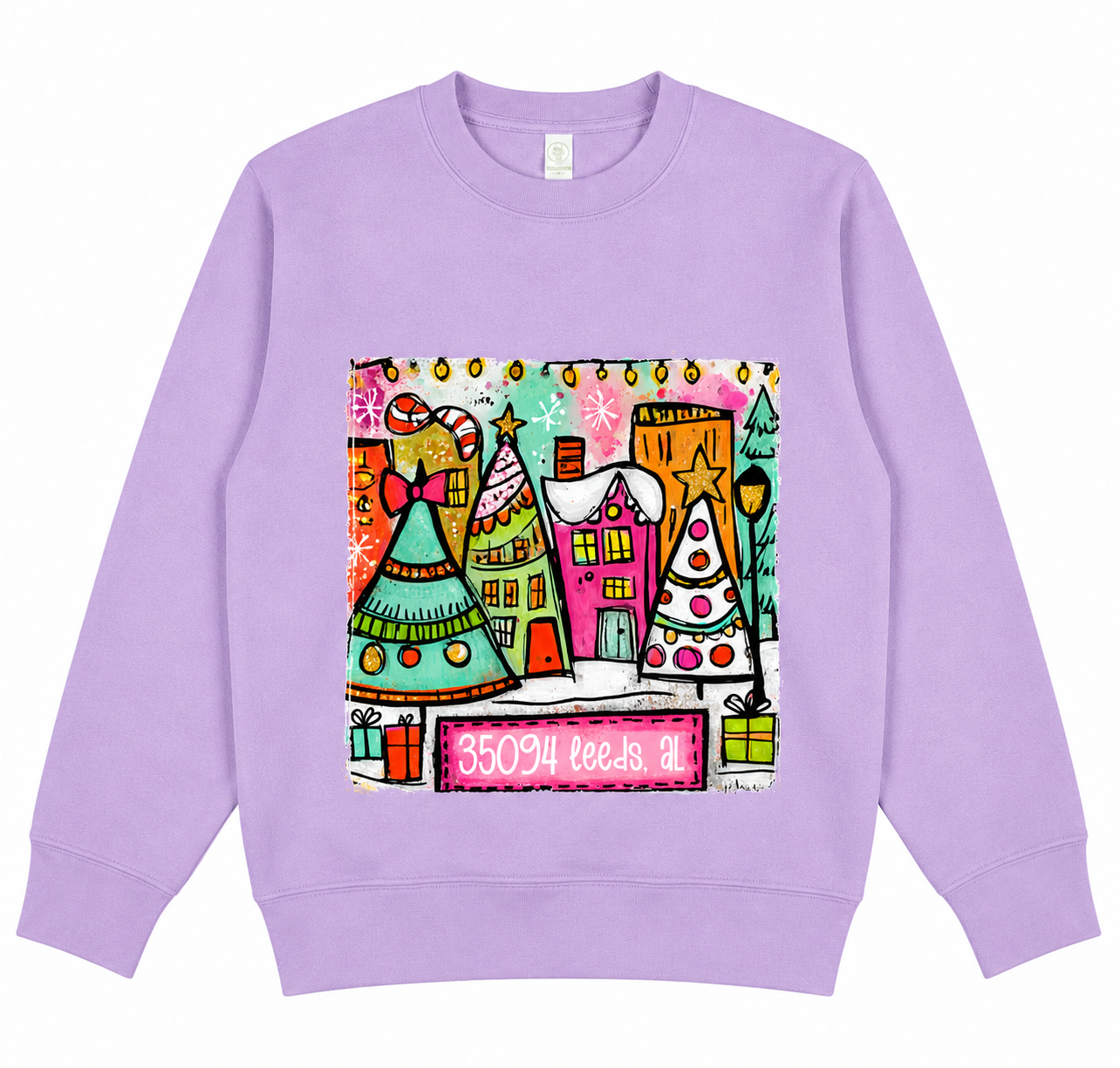 Lavender crewneck sweatshirt featuring a colorful whimsical Christmas village design with decorated trees, festive houses, gifts, and "35094 Leeds, AL" across the front.