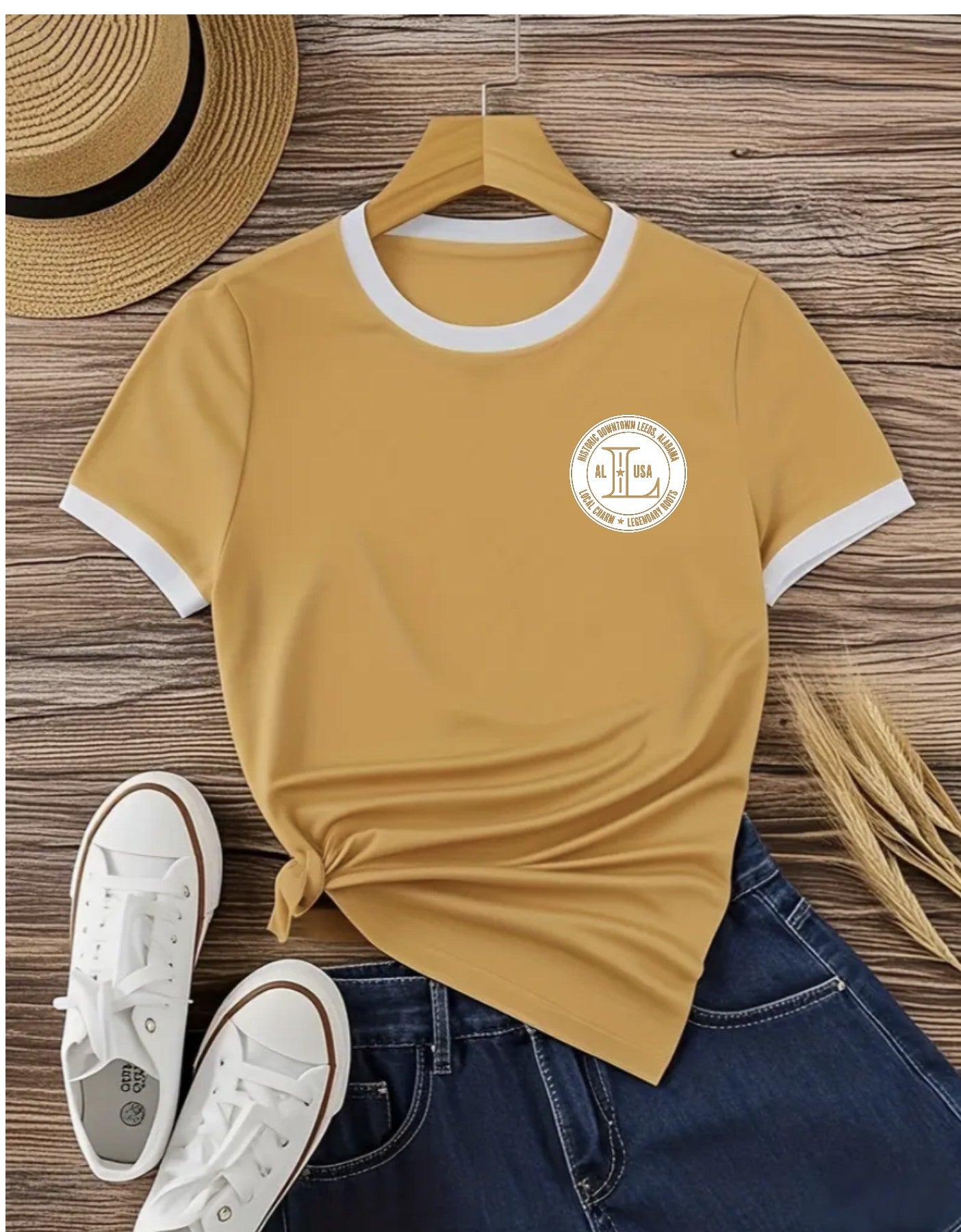 Yellow t-shirt with a logo on a wooden surface with shoes and a hat.
