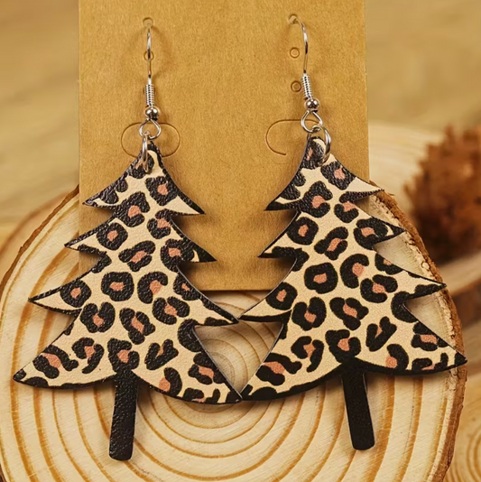 Pair of leopard print Christmas tree PU leather earrings displayed on a wood slice for a rustic holiday look.