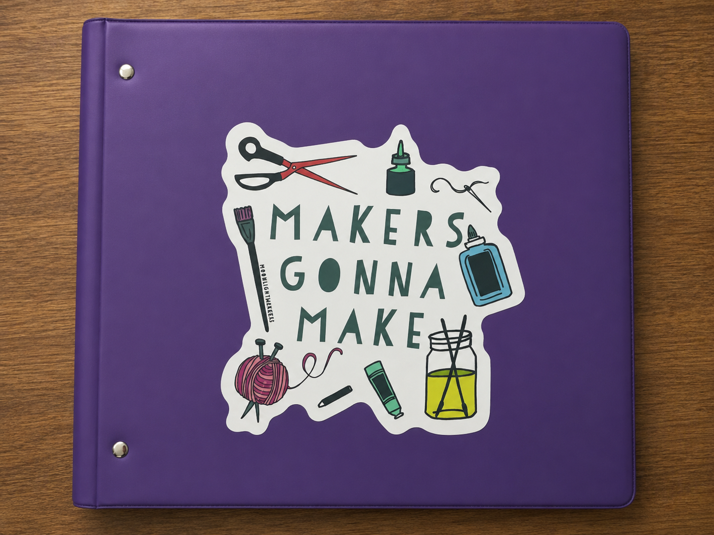 Makers Gonna Make vinyl sticker featuring crafting supplies including scissors, yarn, glue, paintbrush, and sewing needle on a purple binder.