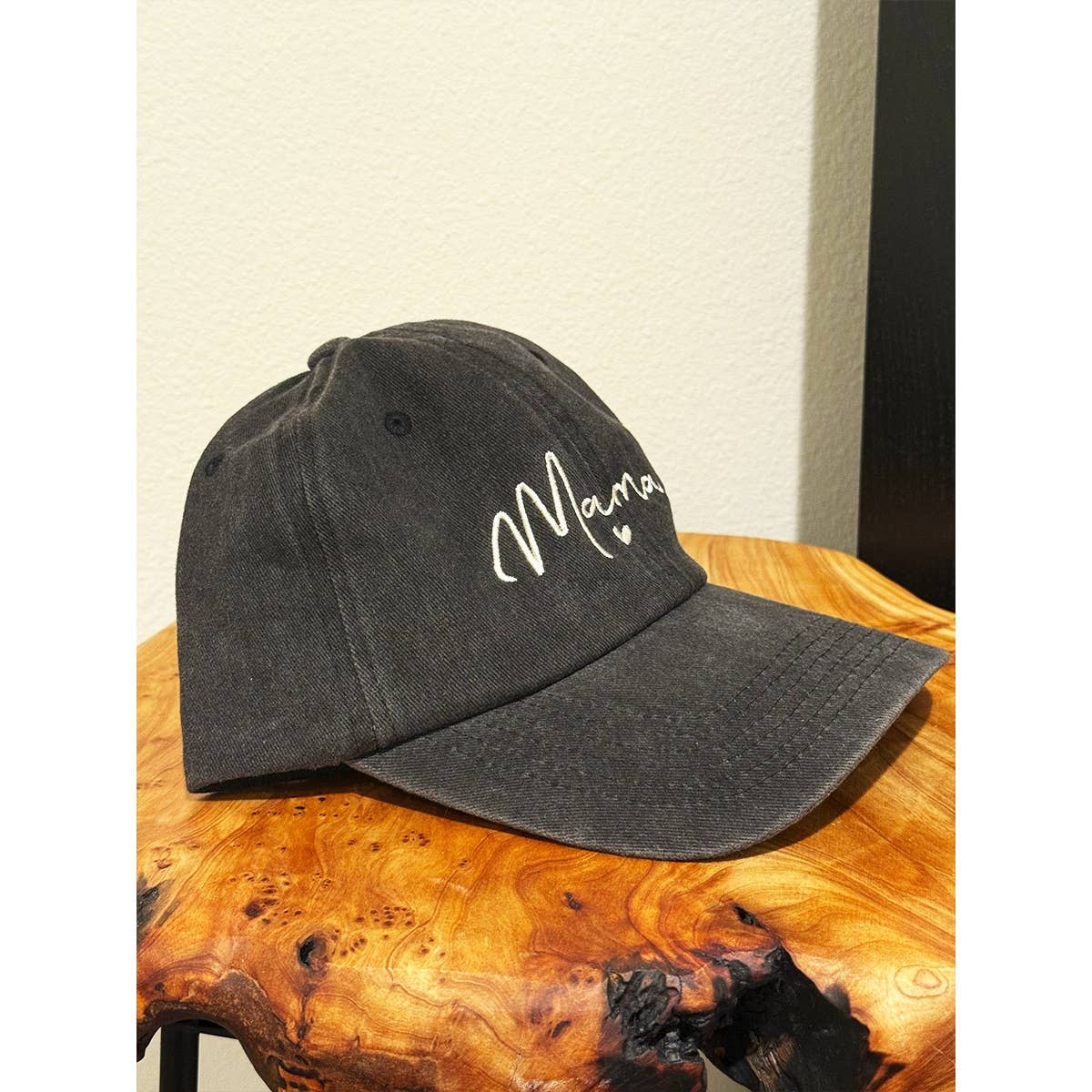 Black cap with 'Mama' embroidery on a wooden surface