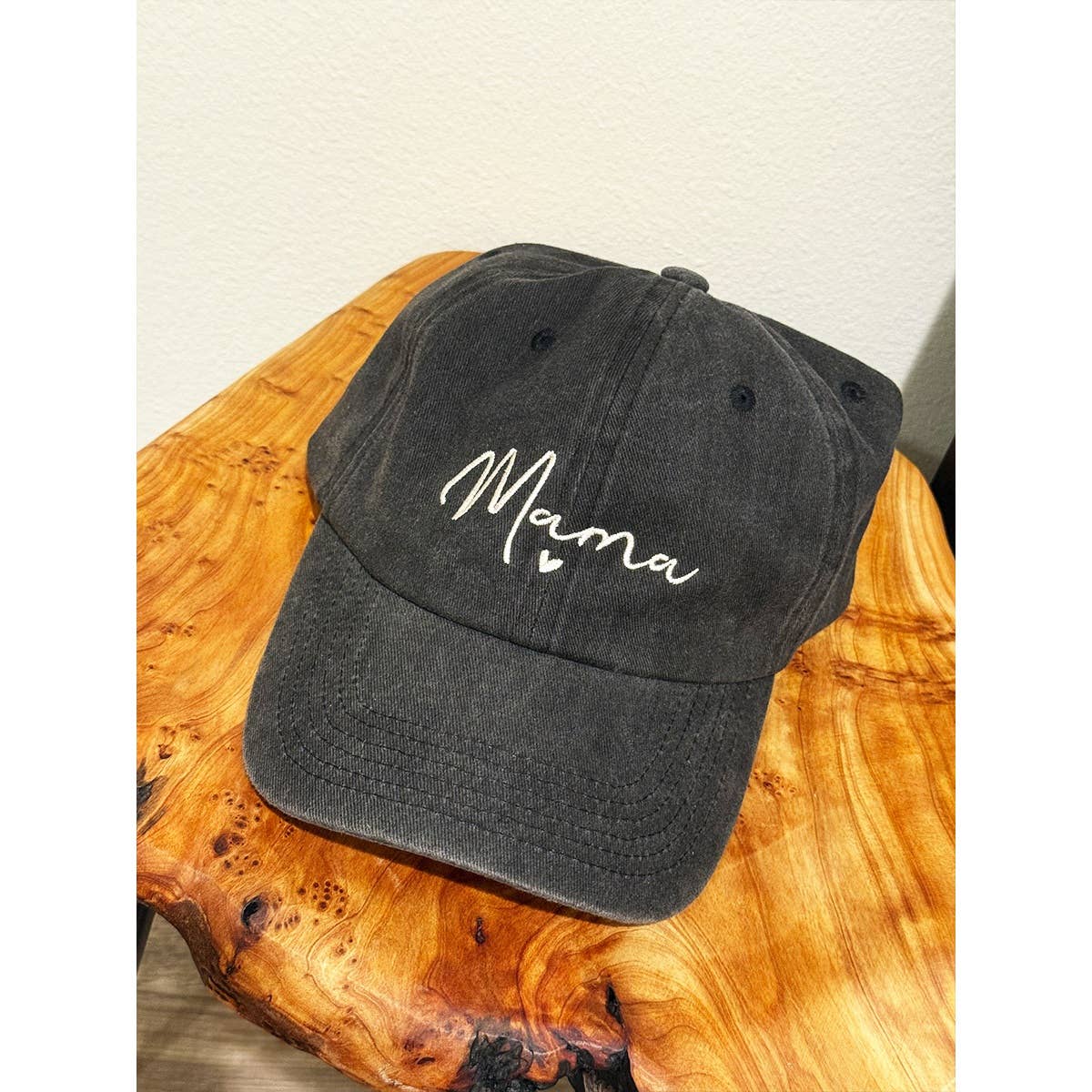 Black cap with 'Mama' text on a wooden surface