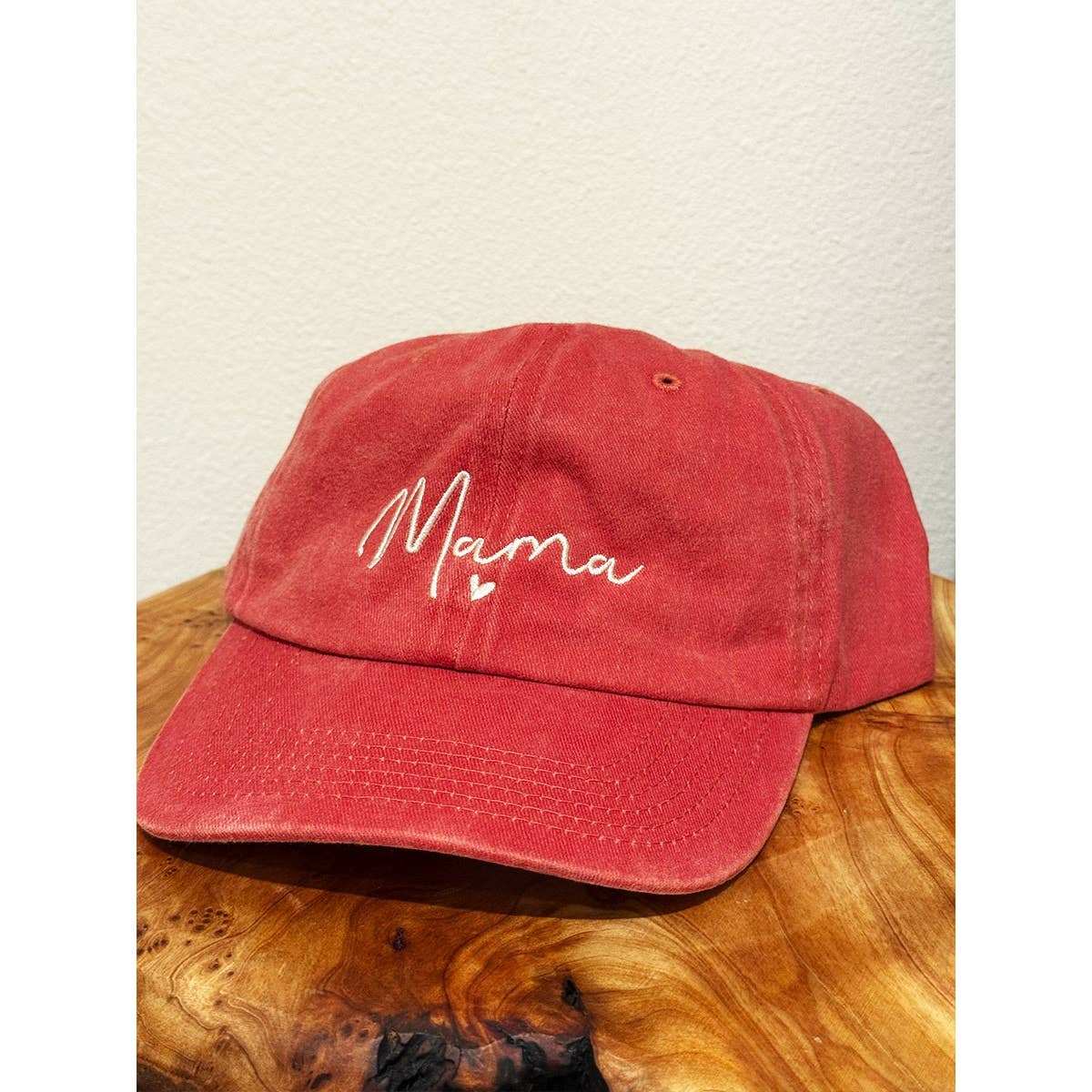 Red cap with 'Mama' embroidery on a wooden surface