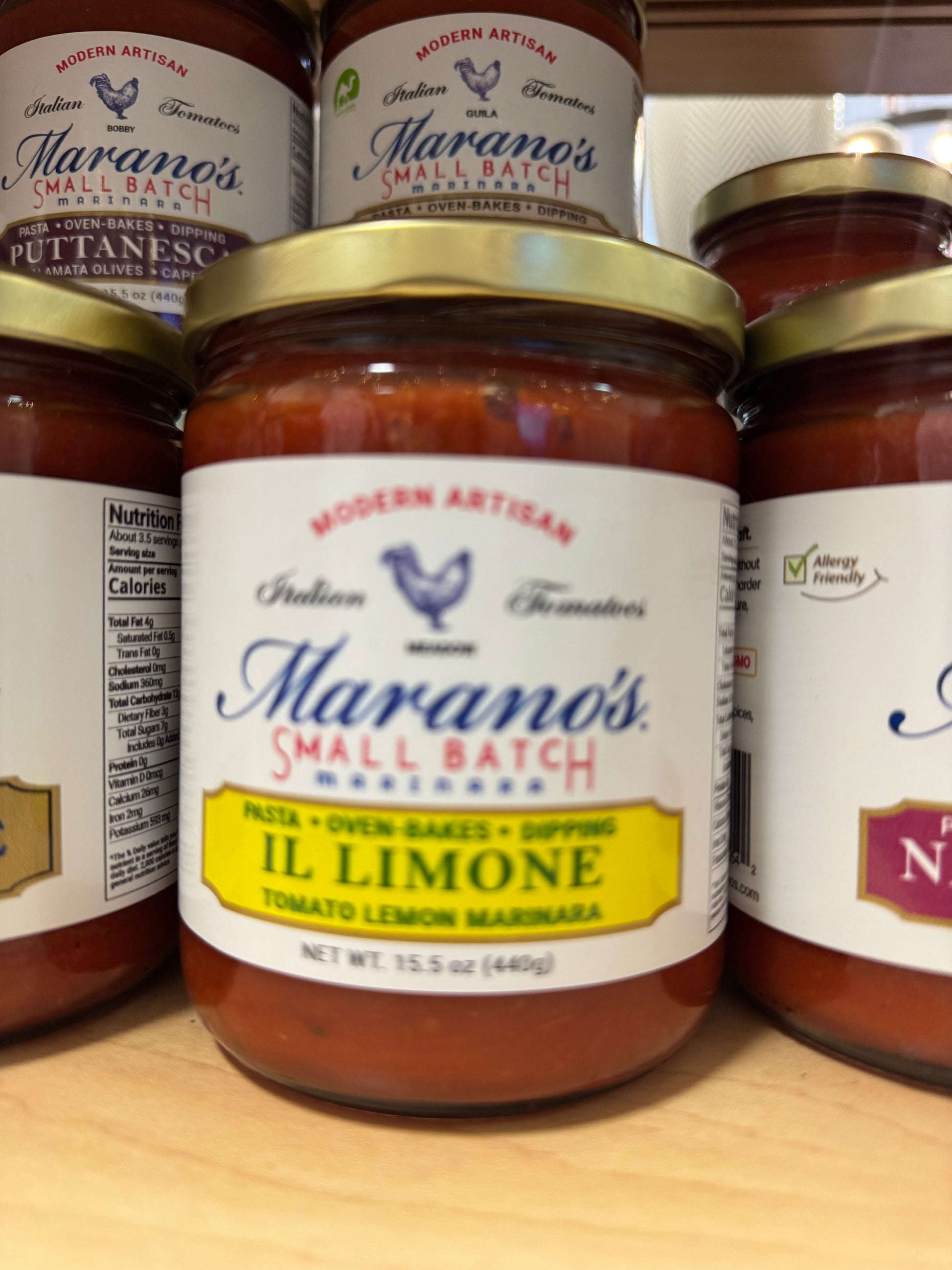 Jar of Marano's Small Batch Il Limone sauce on a wooden surface with other jars in the background.