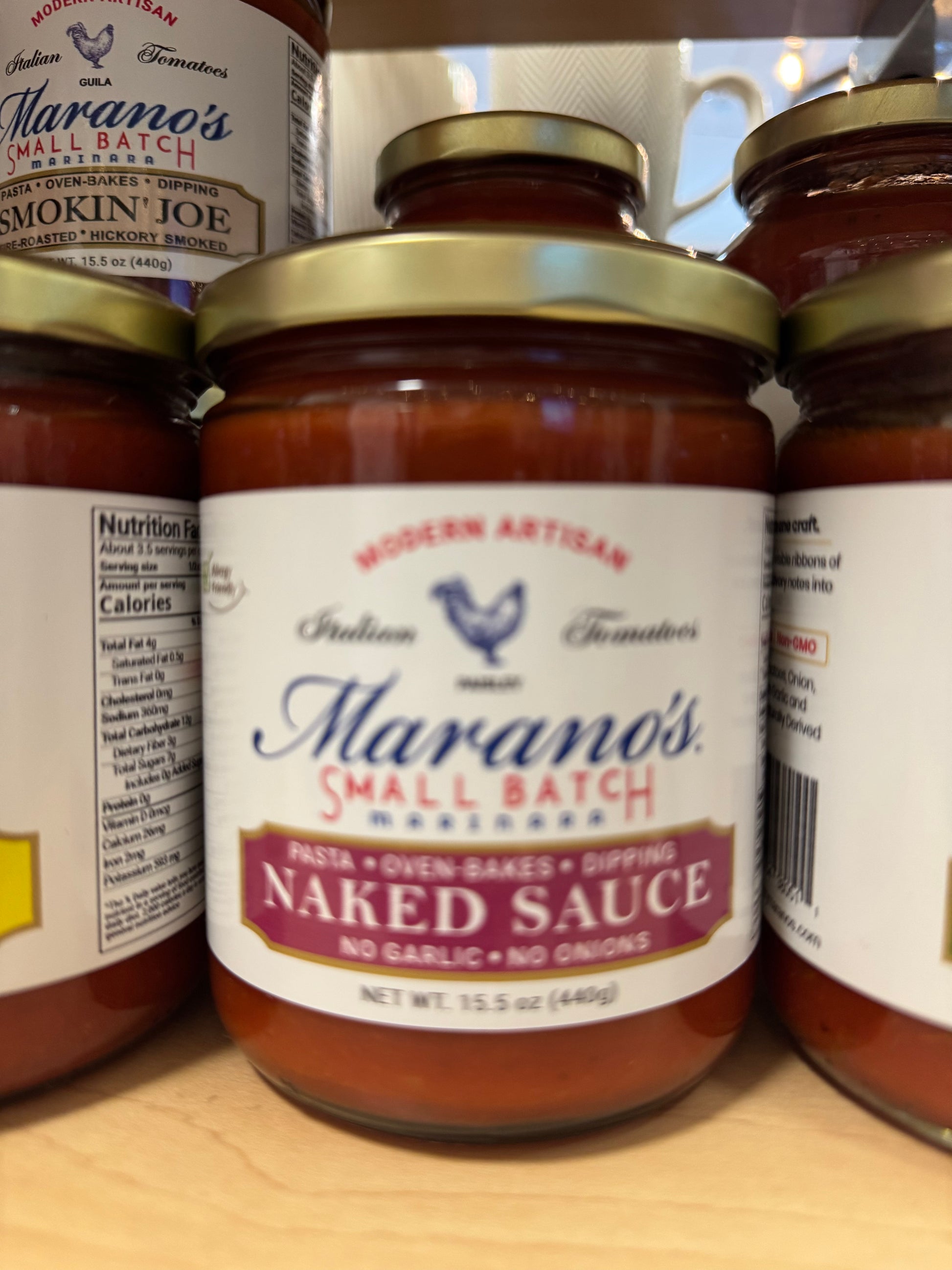 Jar of Marano's Naked Sauce on a wooden surface with other jars in the background.