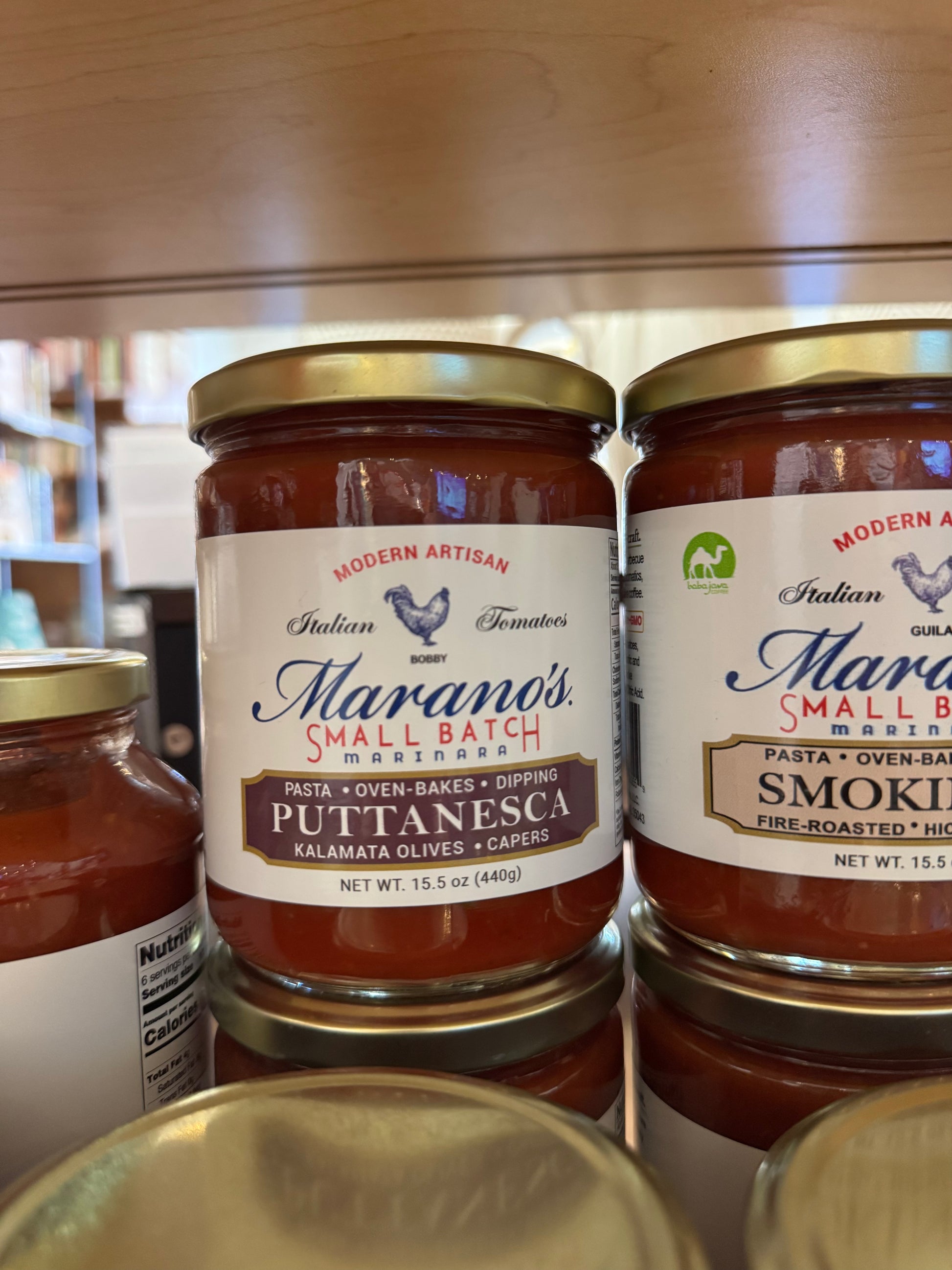 Two jars of Marano's Small Batch pasta sauces on a wooden shelf.