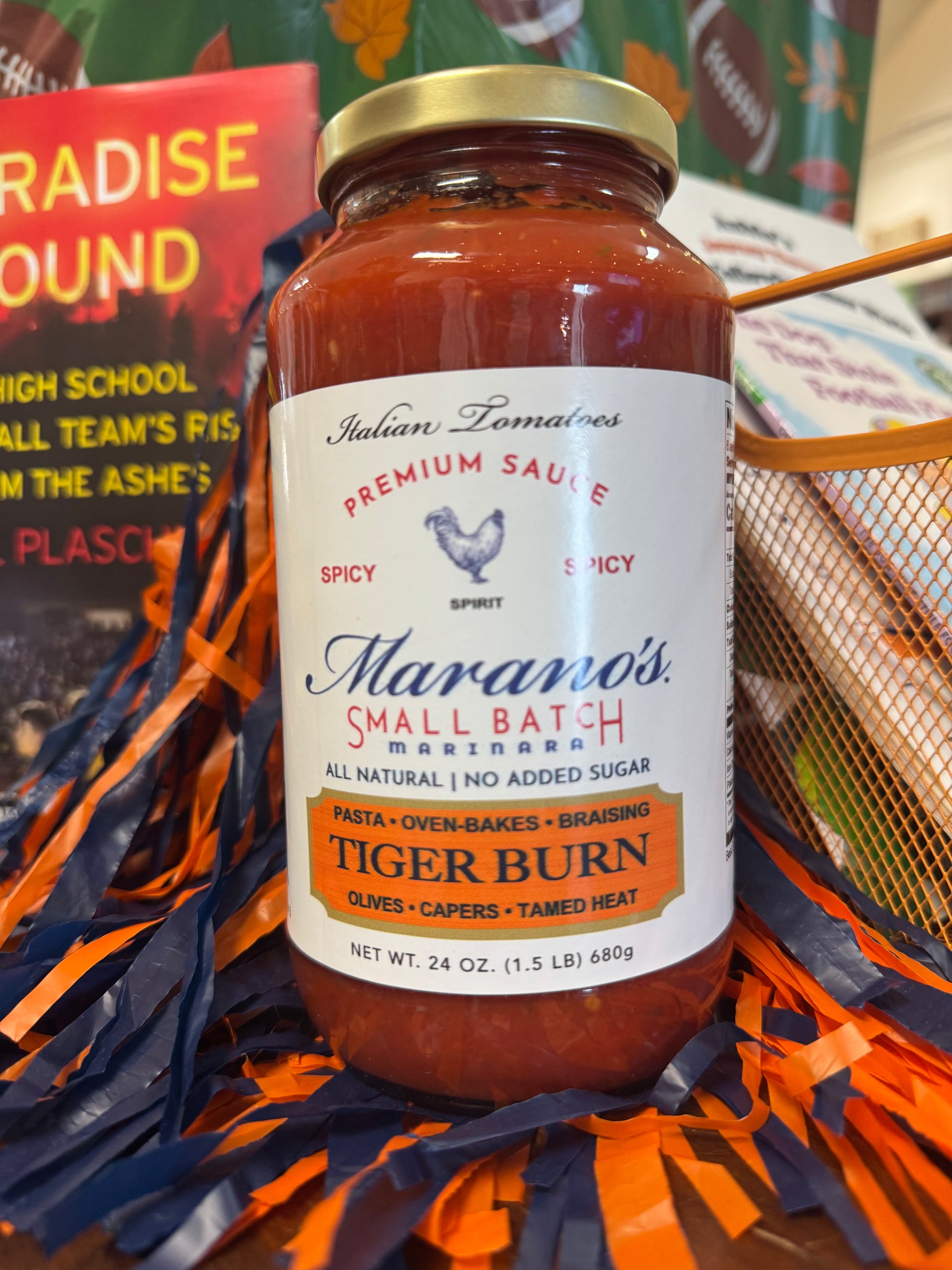Jar of Maramo's Tiger Burn sauce on a sports-themed background with pom-poms.