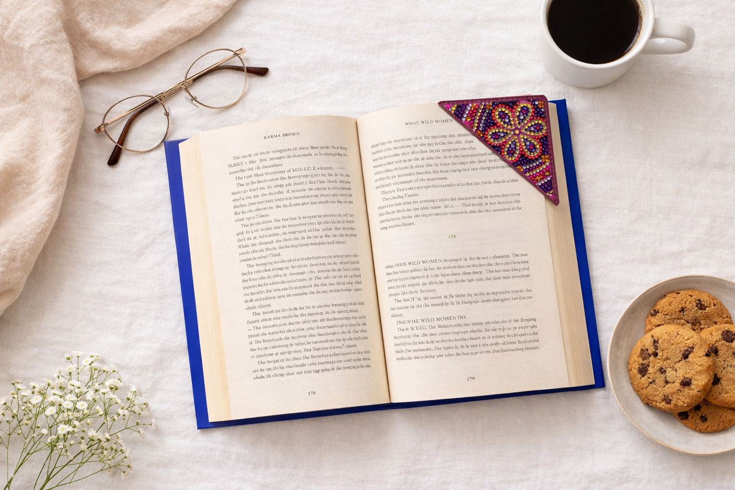 Open book flatlay with reading glasses, coffee, cookies, and colorful bejeweled vegan leather corner bookmark
