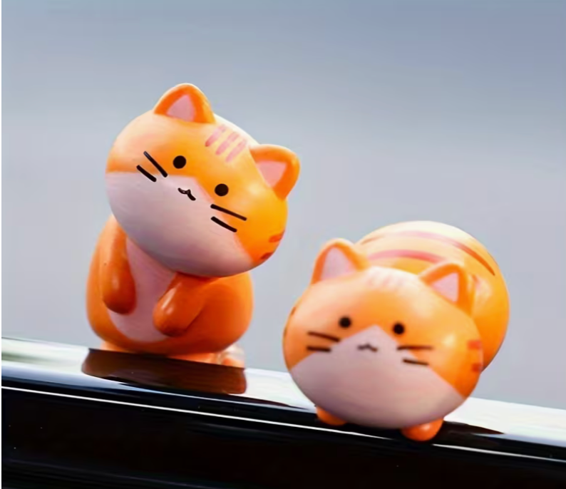 Collection of small orange resin kawaii cat figurines in different poses displayed on a desk with a laptop and mug