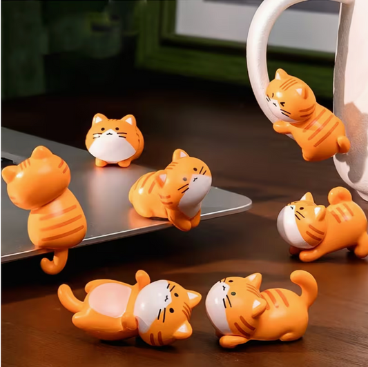 Set of small orange resin kawaii cat figurines in various playful poses displayed on a desk and near a mug, showing miniature size and cute expressions