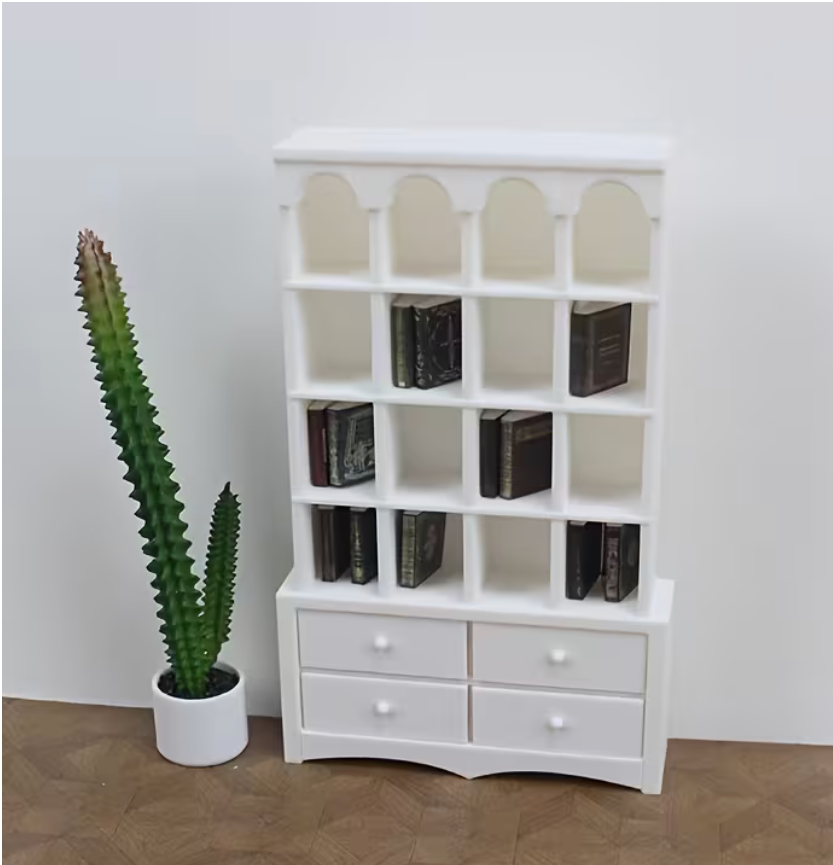 Miniature white bookcase with tiny books displayed on the shelves beside a miniature potted plant.