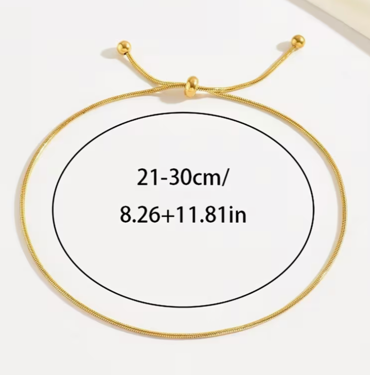 Minimalist gold adjustable anklet with sliding knot closure and delicate dangling ends worn on an ankle