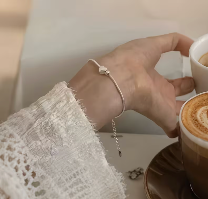 Woman wearing simple silver heart bracelet while holding coffee cup