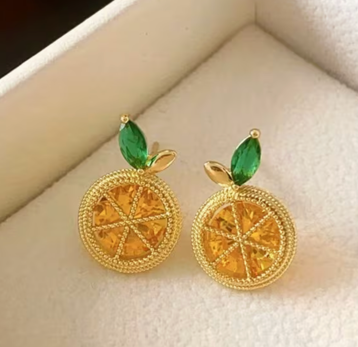 Gold lemon slice stud earrings with green leaf accents displayed in a jewelry box