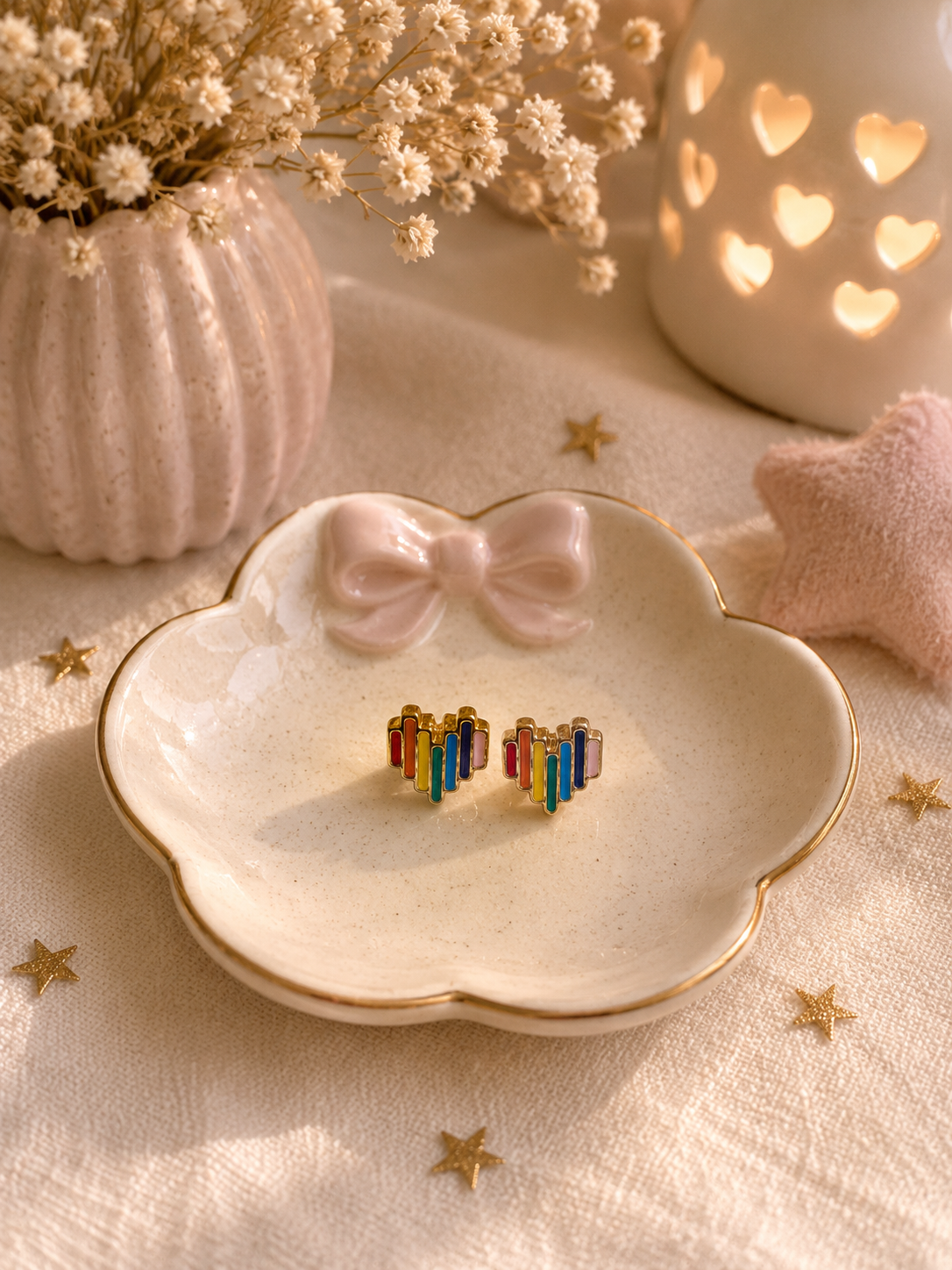 Minimalist rainbow heart stud earrings displayed on ceramic trinket dish with cozy neutral decor