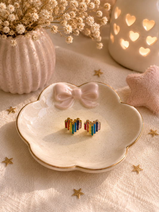 Minimalist rainbow heart stud earrings displayed on ceramic trinket dish with cozy neutral decor
