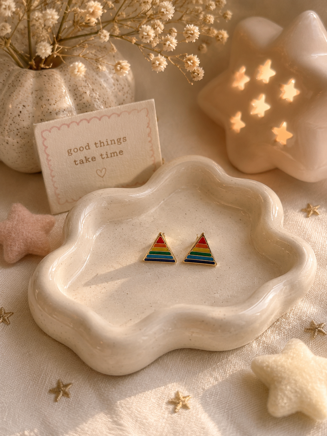 Minimalist rainbow triangle stud earrings displayed on cream ceramic trinket dish with cozy decor