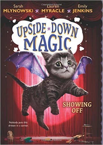 Book cover of 'Upside Down Magic' with a cat wearing butterfly wings against a red curtain background.