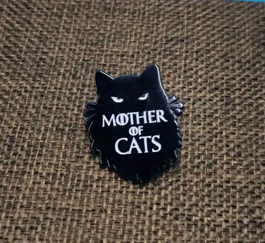Mother of Cats enamel pin featuring a sleek black cat silhouette with bold white lettering on a burlap background