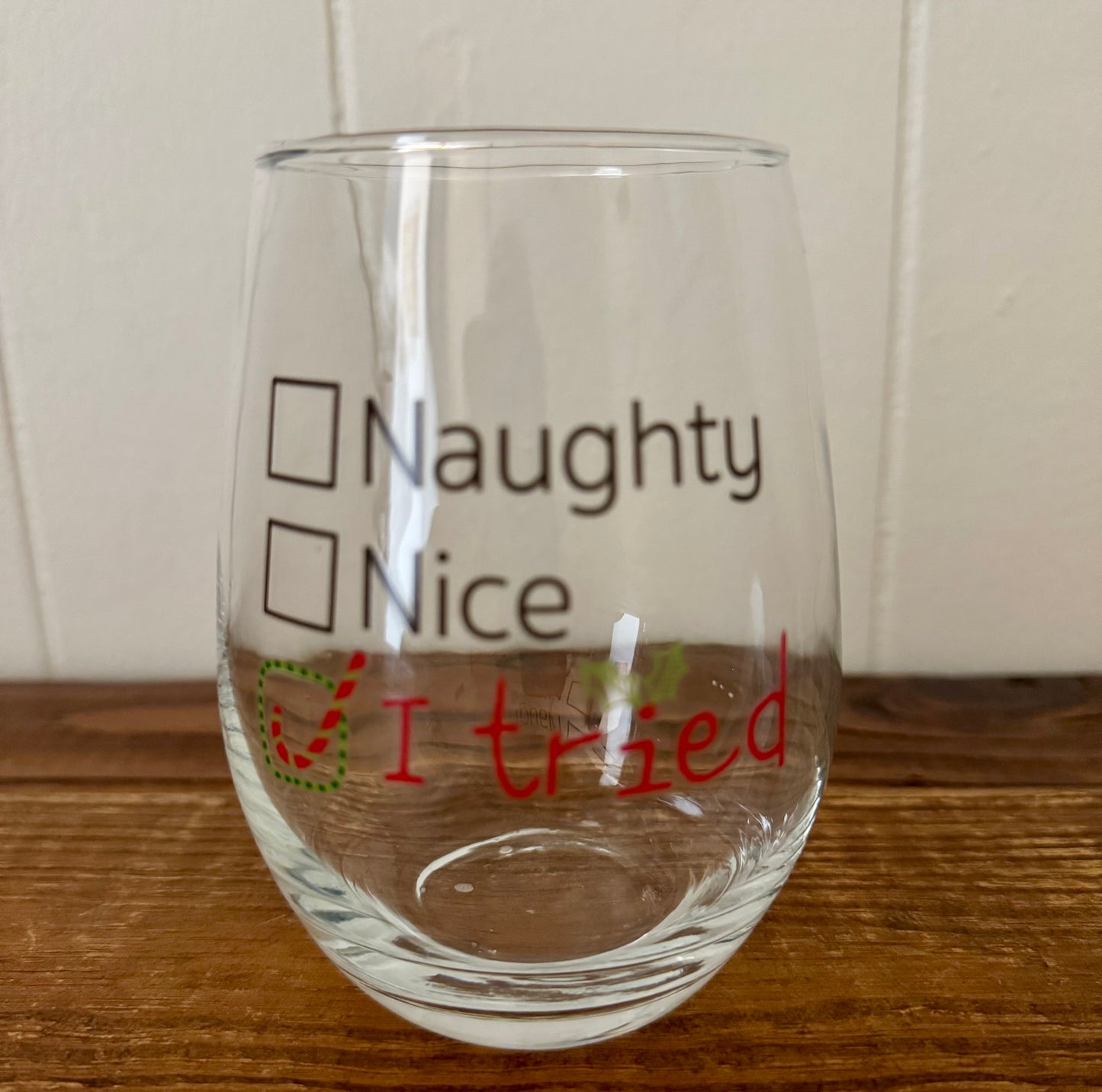 Clear glass with text 'Naughty', 'Nice', and 'I tried' on a wooden surface.