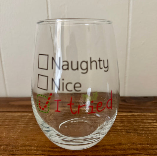 Clear glass with text 'Naughty', 'Nice', and 'I tried' on a wooden surface.