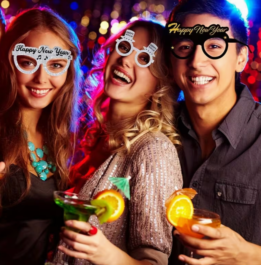 three people wearing Happy New Year glitter glasses at a party holding drinks and smiling