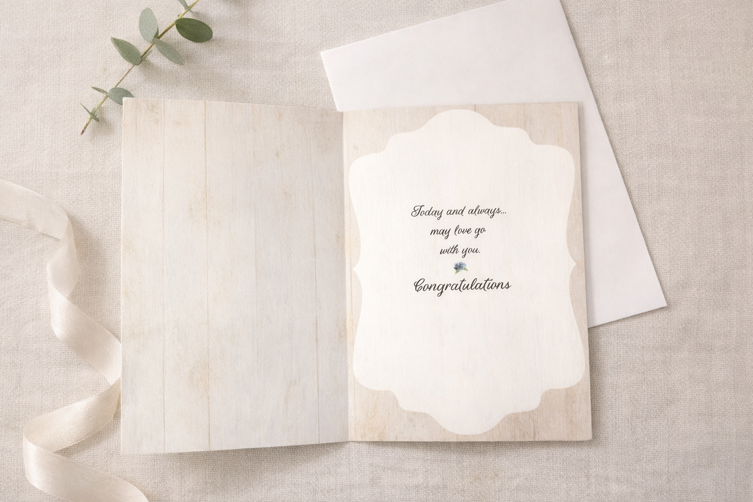 Open wedding greeting card showing inside message that reads Today and always may love go with you, Congratulations, styled on a neutral linen flat lay with white envelope, ribbon, and eucalyptus.