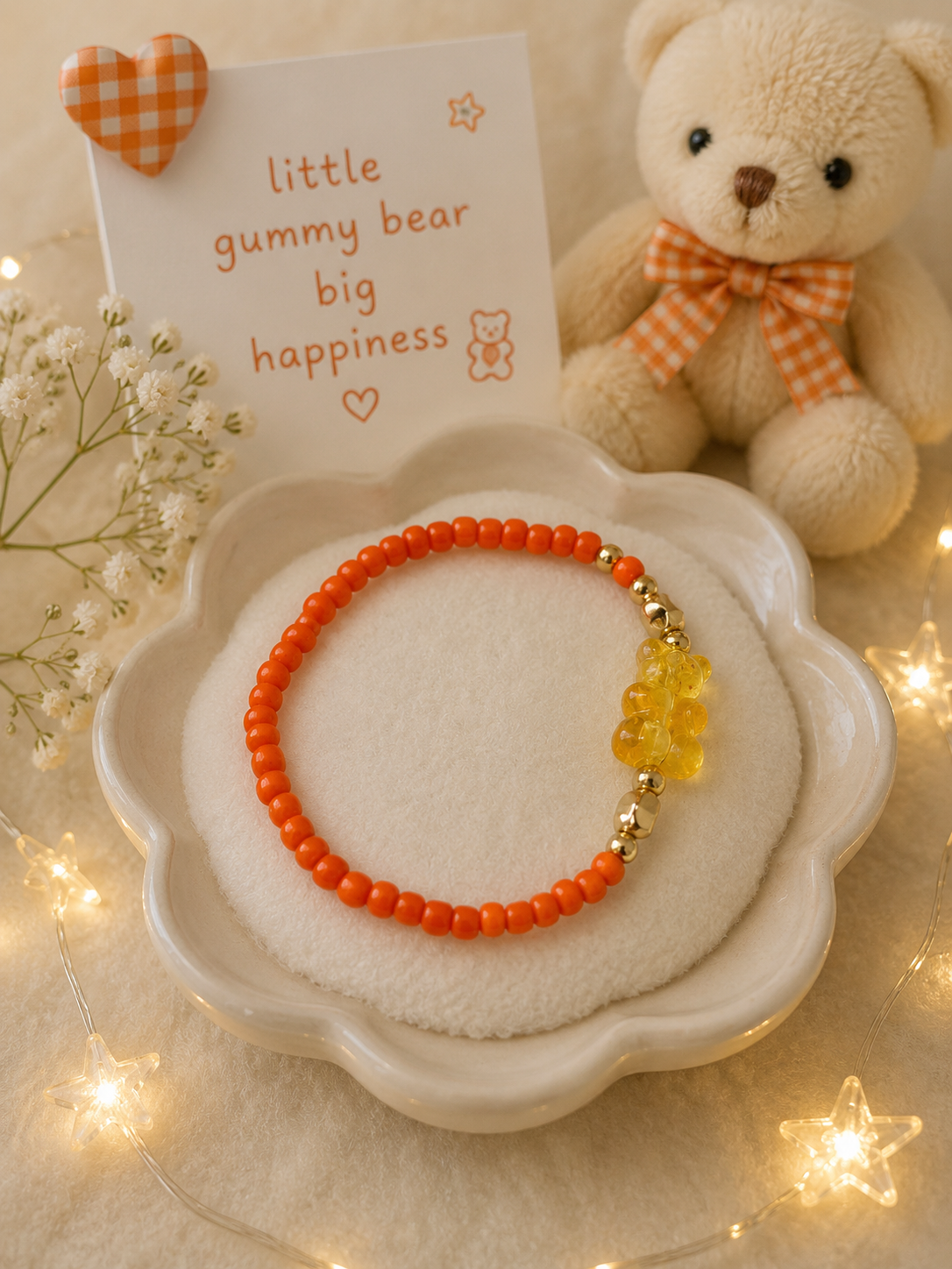 Orange stretch bead bracelet with transparent gummy bear charm and gold accents displayed with teddy bear decor