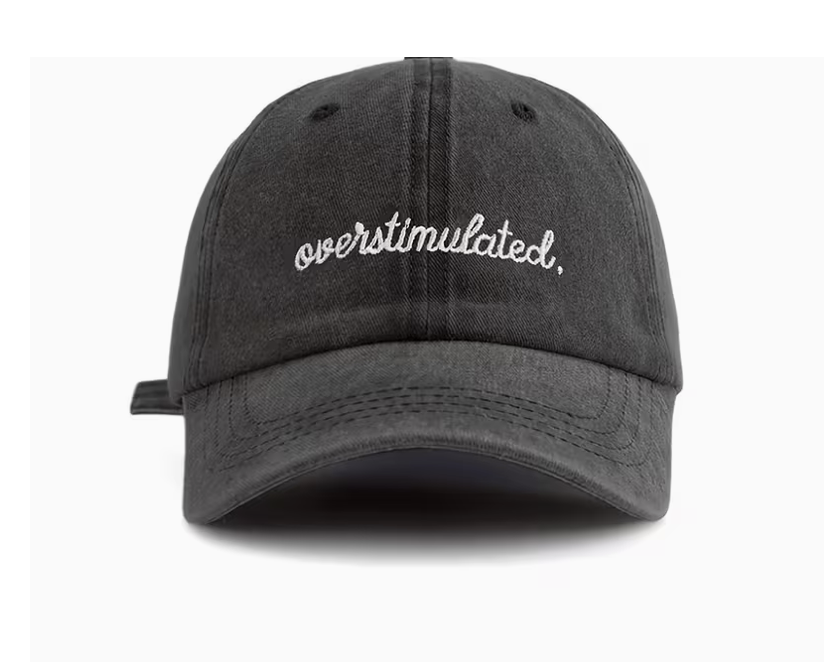 A dark gray washed cotton baseball cap with 'overstimulated.' embroidered in white script across the front, shown against a plain white background.