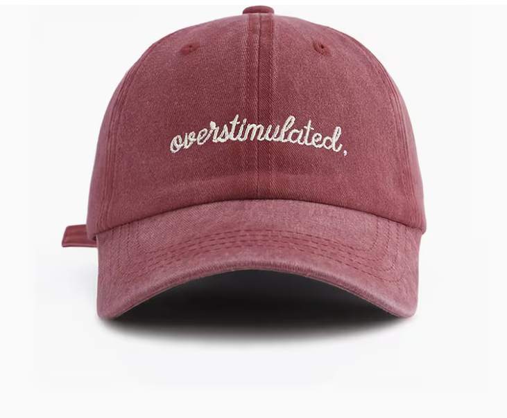 A washed dusty rose baseball cap with 'overstimulated.' embroidered in white script across the front, shown against a plain white background.