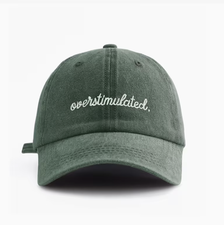 A dark green washed cotton baseball cap with 'overstimulated.' embroidered in white script across the front, shown against a plain white background.