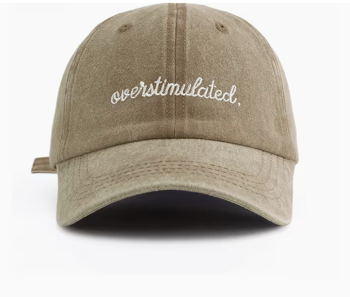 A washed tan baseball cap with 'overstimulated.' embroidered in white script across the front, shown against a plain white background.